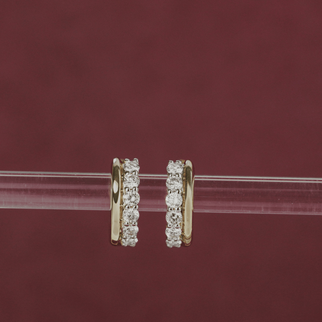14k gold diamond huggie and plain huggie earrings showcased on a clear bar, centered in the frame. 