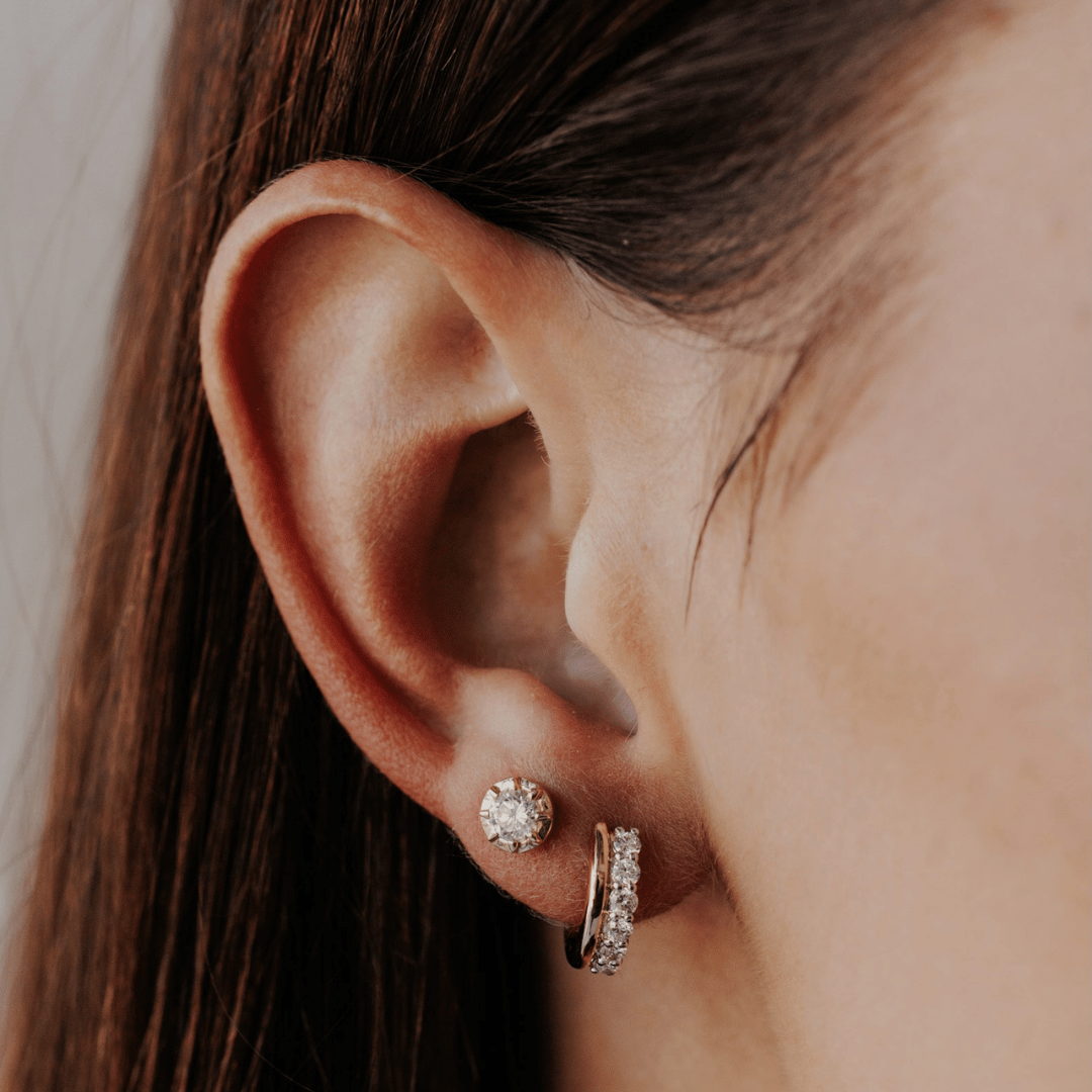 14k gold diamond huggie and plain huggie earrings showcased on a the ear of a model. 
