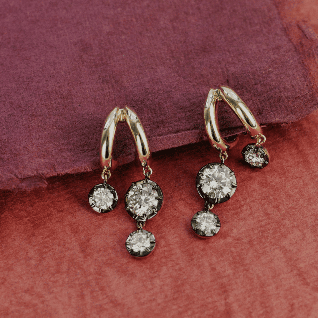 14k gold double hoop, round cut, lab grown diamond dangle earrings with Black Rhodium featured on a textured red surface.  