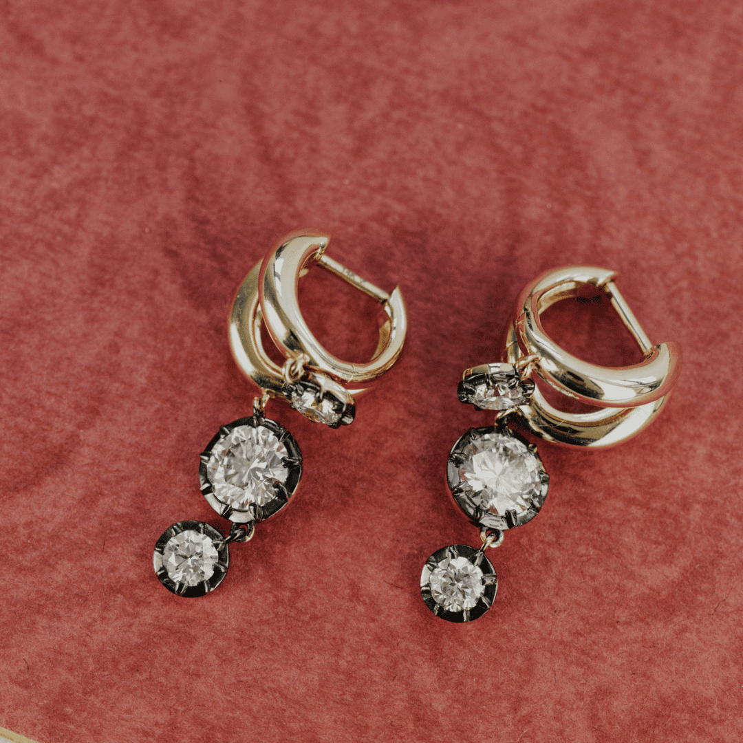 14k gold double hoop, round cut, lab grown diamond dangle earrings with Black Rhodium featured on a textured red surface.  