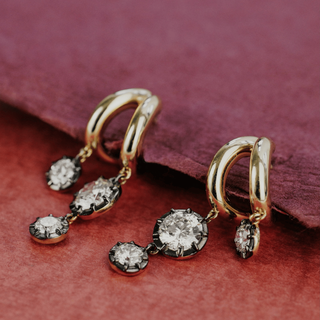 14k gold double hoop, round cut, lab grown diamond dangle earrings with Black Rhodium featured on a textured red surface.  