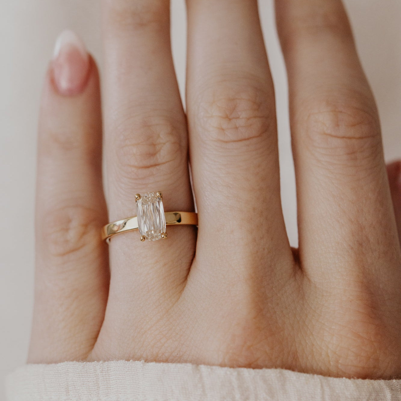 Gold Octavia ring with a champagne diamond on a person's finger against a neutral background.