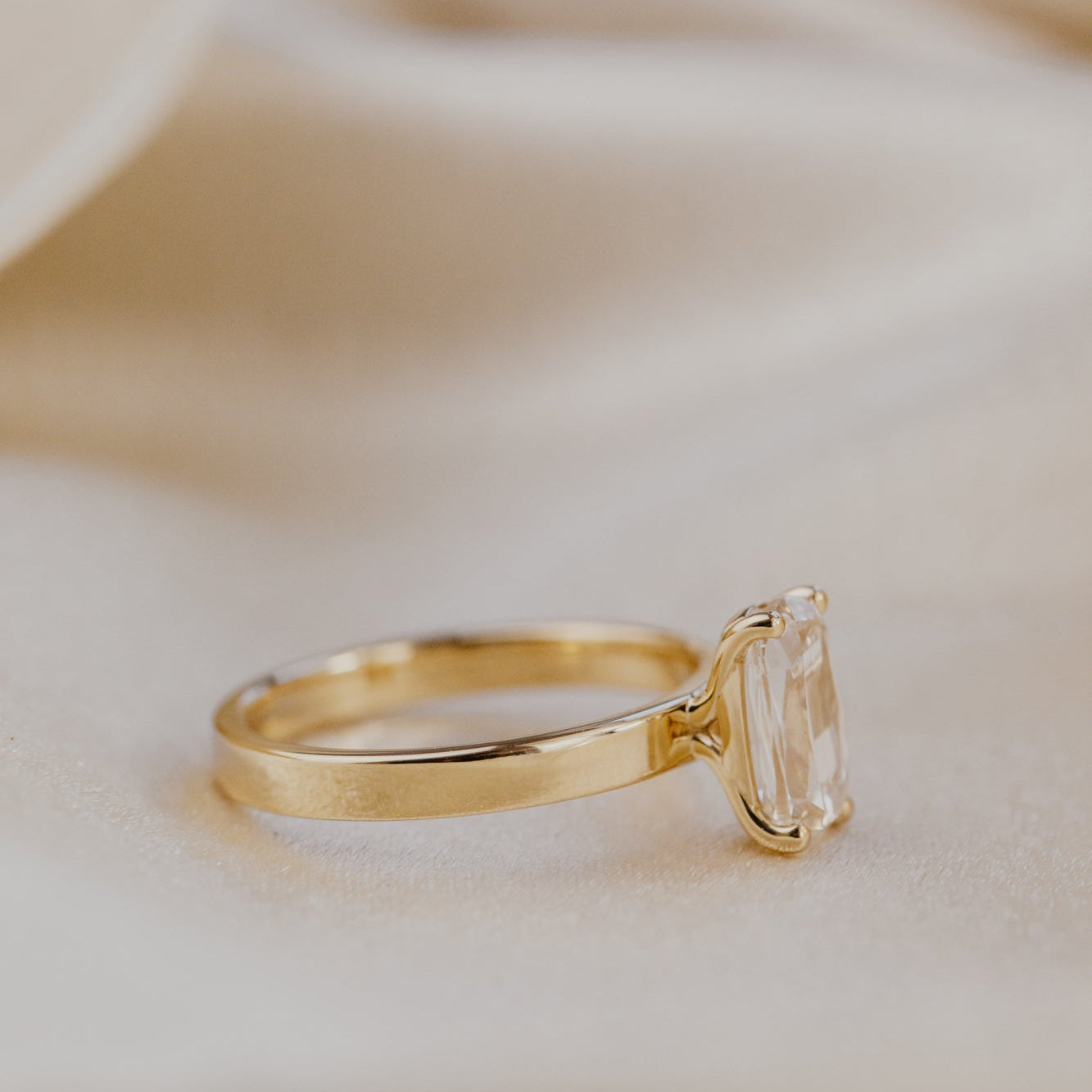 Gold ring with a elongated cushion champagne diamond on a soft beige background.