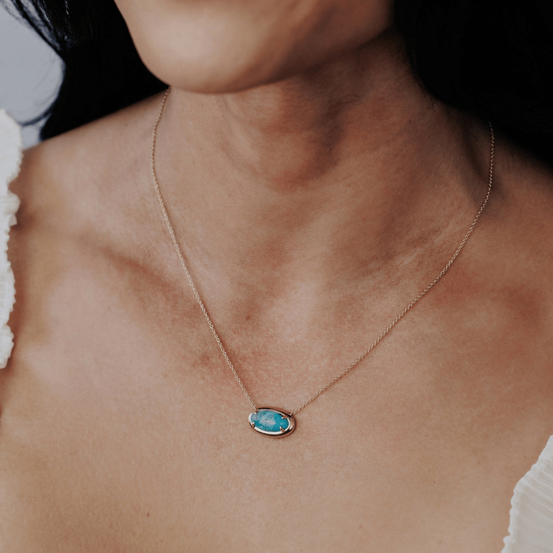 A 14k gold, elongated oval turquoise necklace in a metal border setting on the neck of a model.
