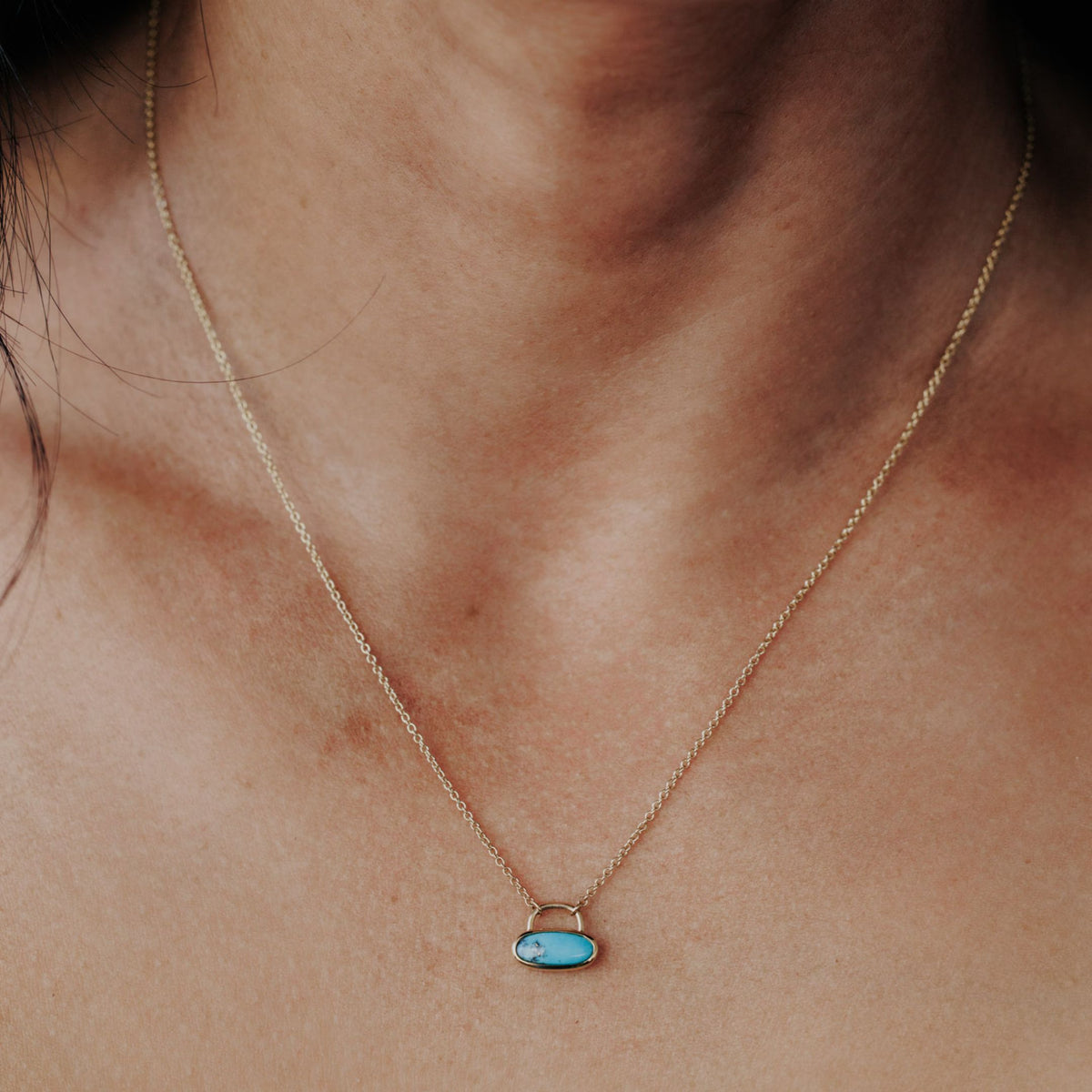 A 14k yellow gold  turquoise necklace with a lock style design set on the neck of a model. 