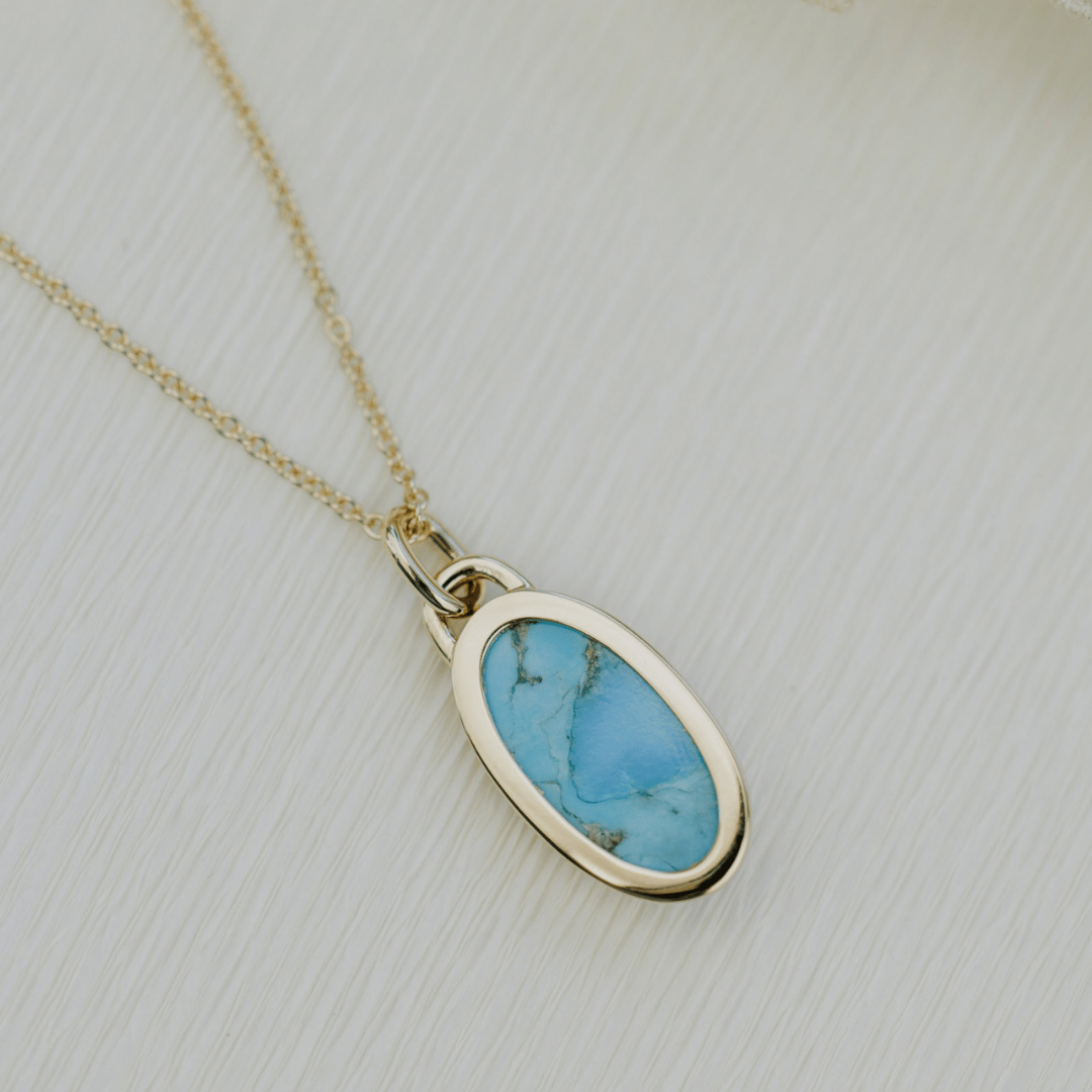 The backside of a 14k yellow gold elongated turquoise necklace on a soft white background. 