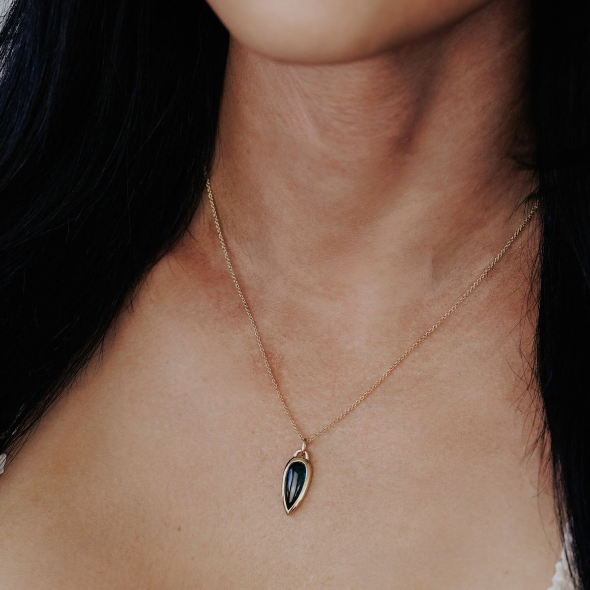 A 14k gold necklace with an elongated pear shaped green tourmaline stone on the neck of a model. 