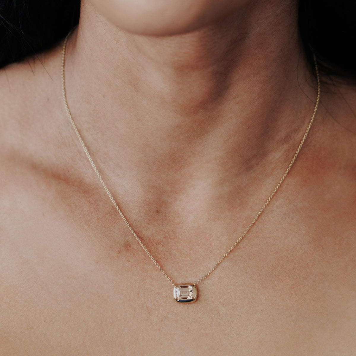 An emerald cut morganite necklace in a gold setting set on the neck of a model. 