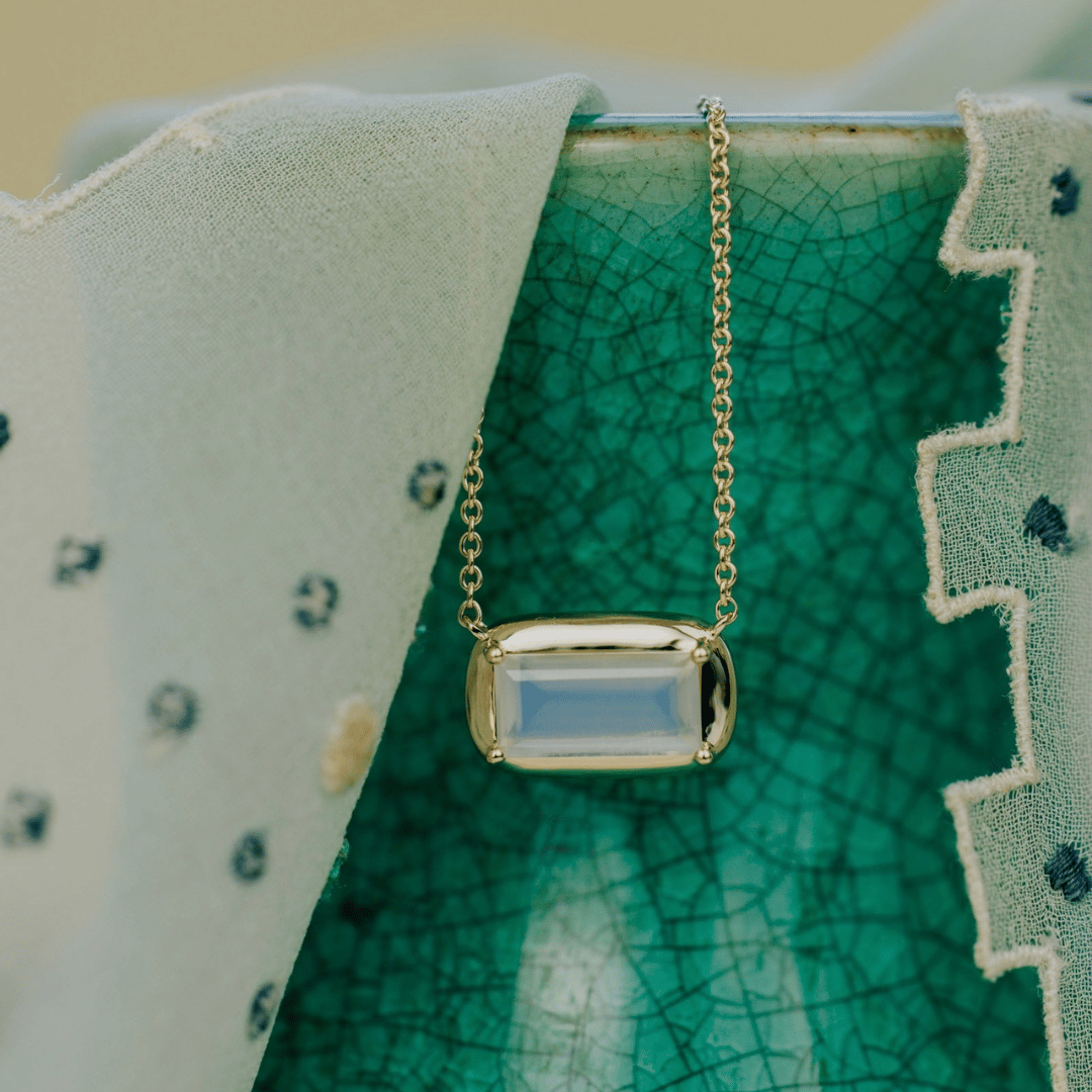 A 14k yellow gold emerald cut moonstone necklace on a textured background. 