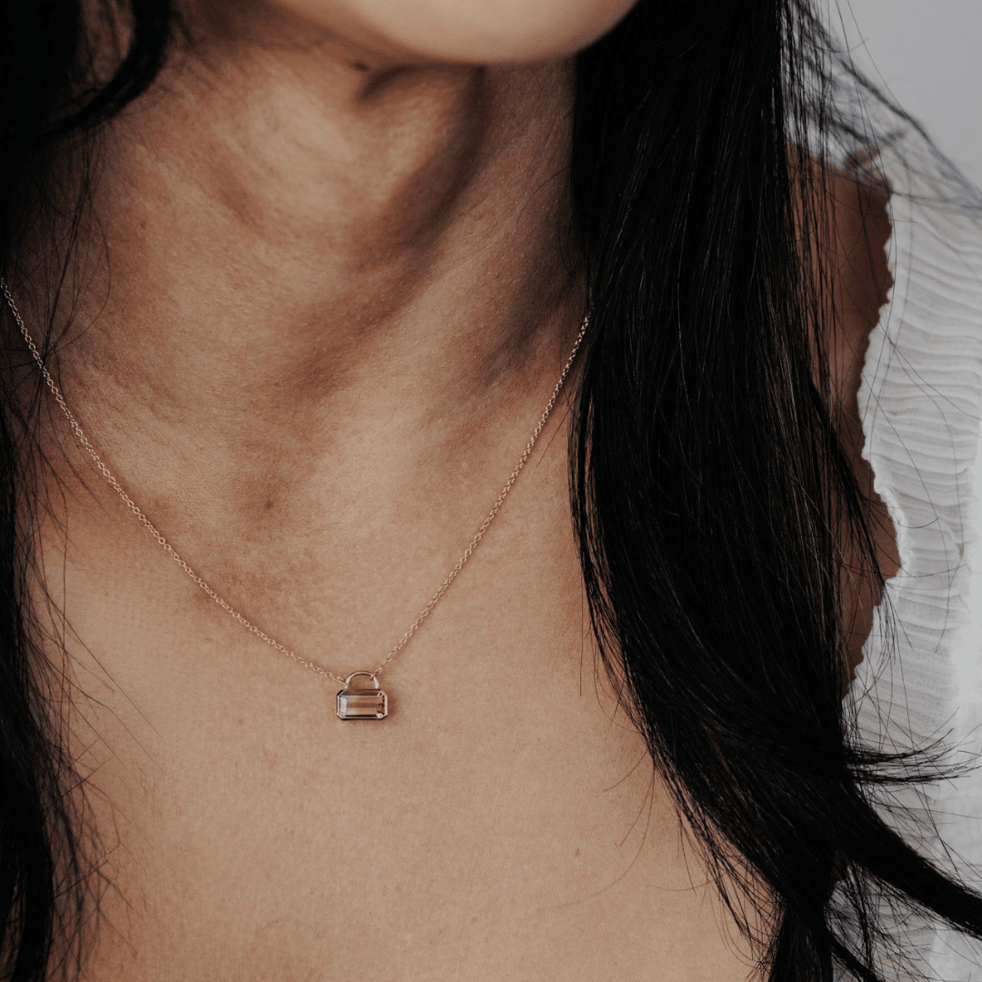 A 14k yellow gold emerald-cut, pink tourmaline stone in a lock style design on the neck of a model. 