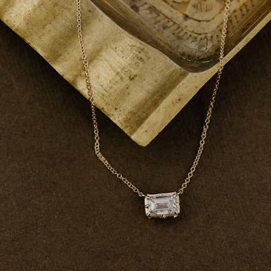 Gold necklace with a lab grown diamond pendant on a textured surface.