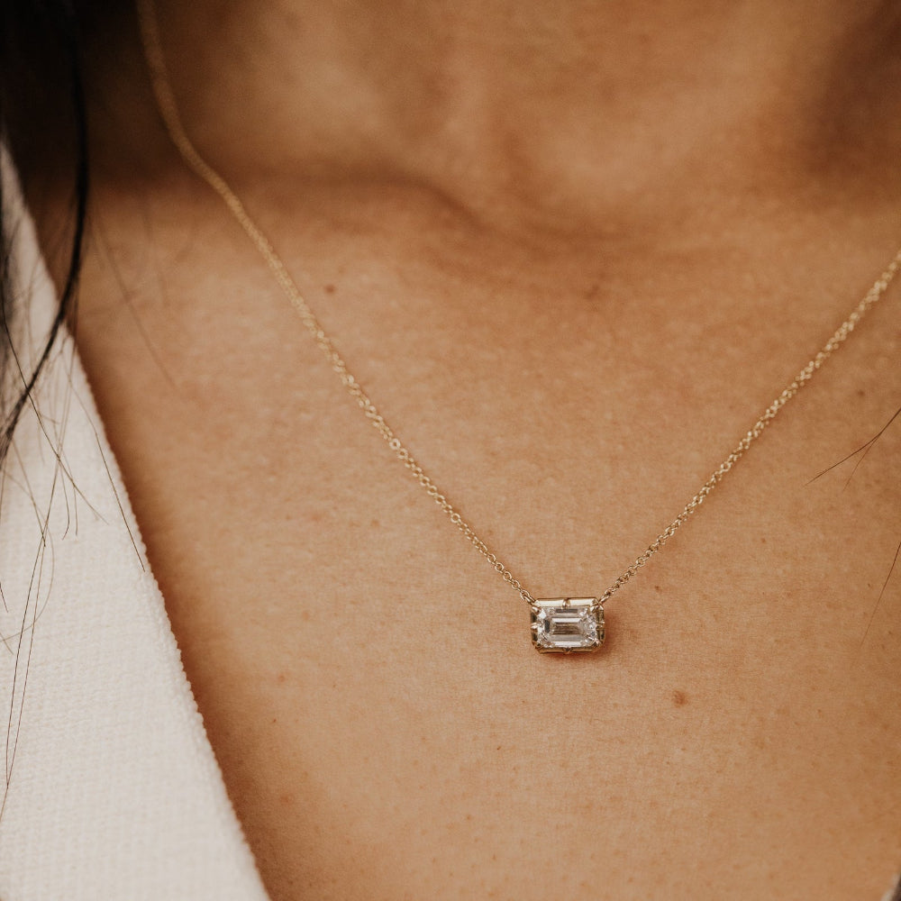 Gold necklace with a lab grown diamond pendant on a person's neck.