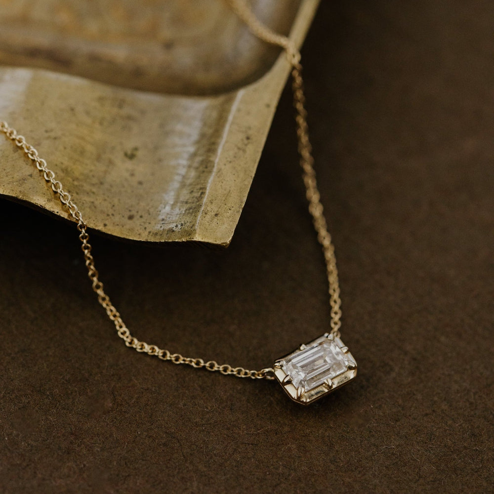 Gold necklace with a lab grown diamond pendant on a textured brown surface.