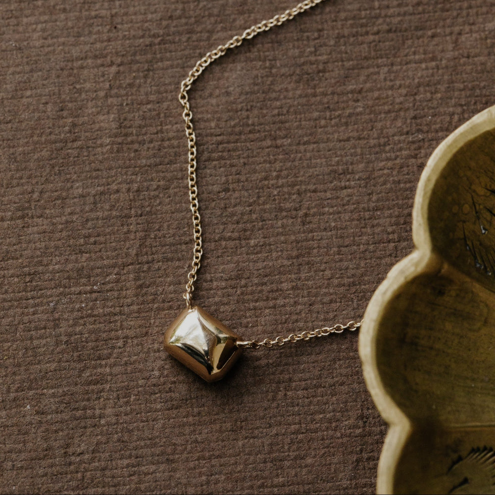 Gold necklace with a geometric pendant on a brown textured surface.
