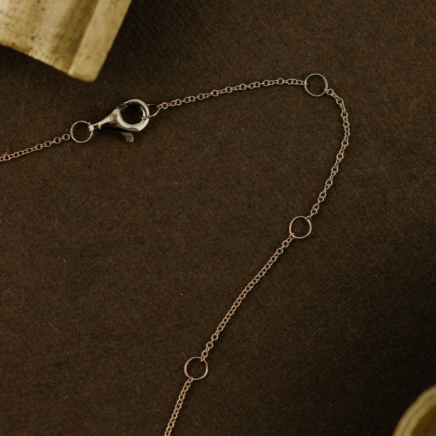 Gold chain necklace on a dark brown surface with an ornate box in the background.