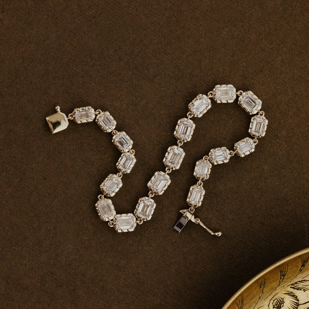 Yellow gold bracelet with emerald cut lab grown diamonds on a brown surface.