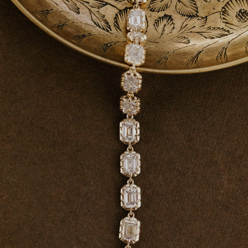 Diamond tennis bracelet with emerald cut lab grown diamonds on a textured brown surface.