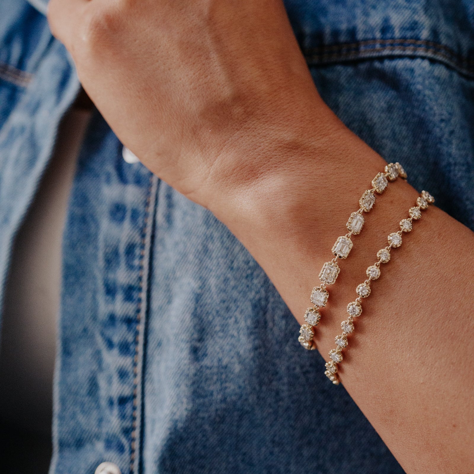 Close-up of a person wearing a gold tennis  bracelet against a denim background.