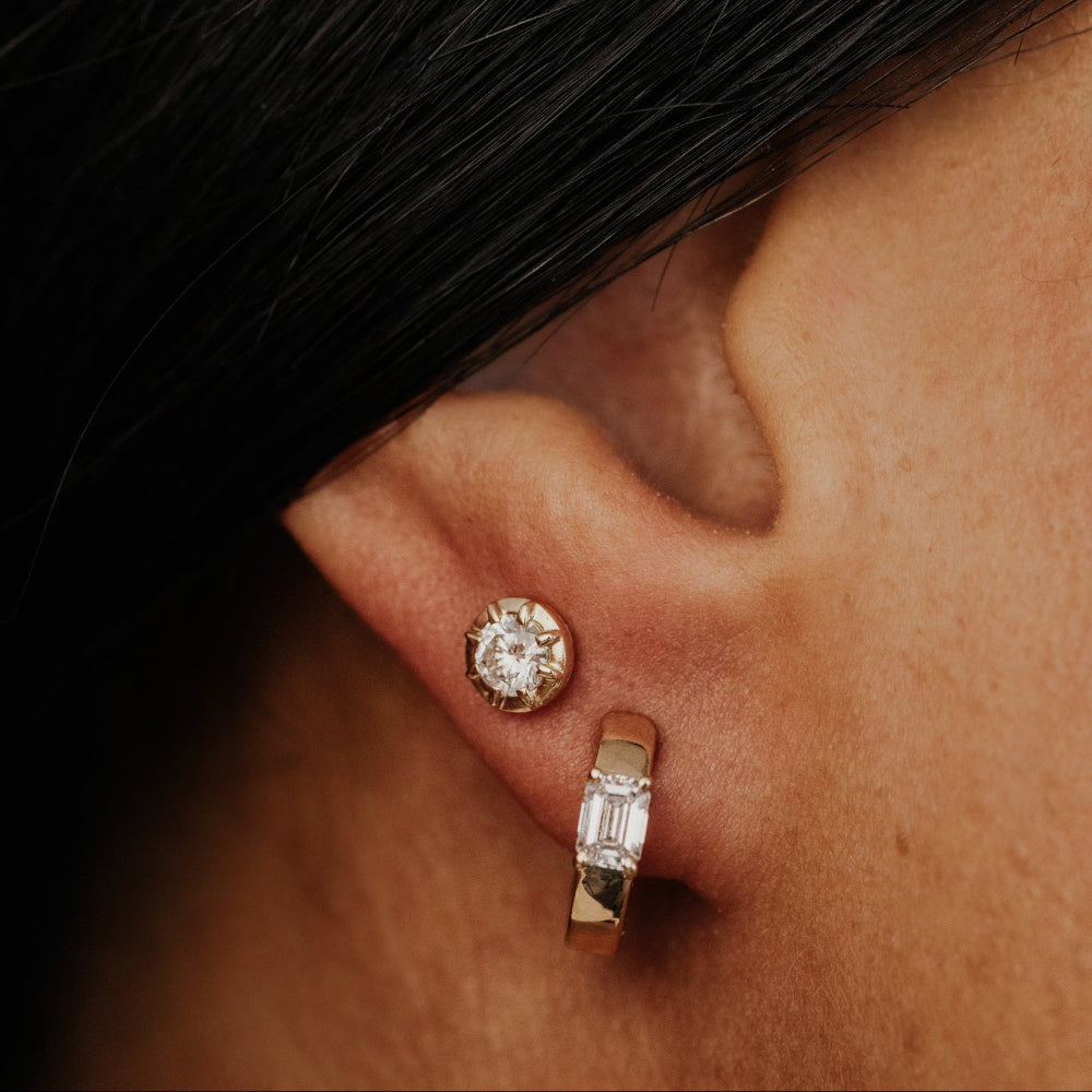 Close-up of a person wearing yellow gold hoop earrings with emerald cut lab grown diamonds and a round lab grown diamond stud earrings.