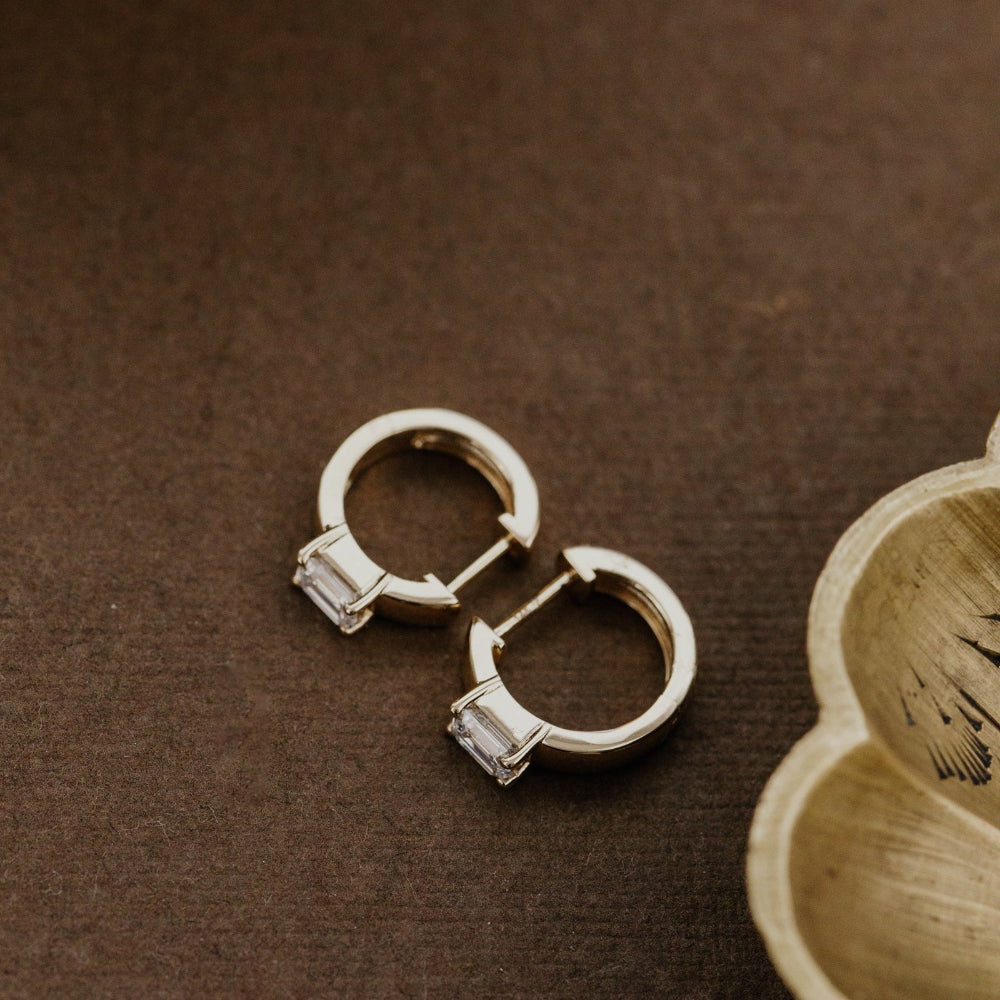 Yellow gold lab grown diamond hoop earrings on a brown surface with a bowl in the background.