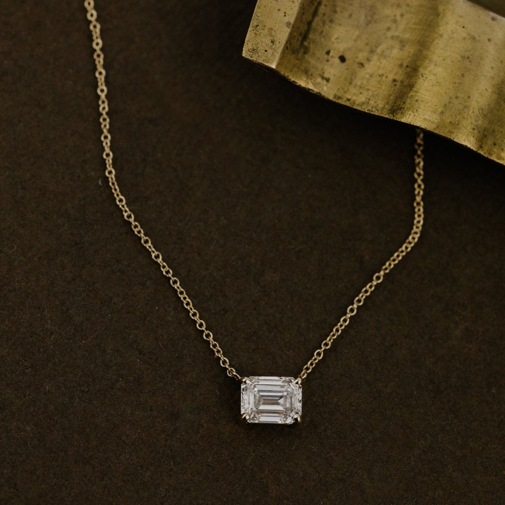 Gold necklace with a emerald cut lab grown diamond pendant on a dark surface.