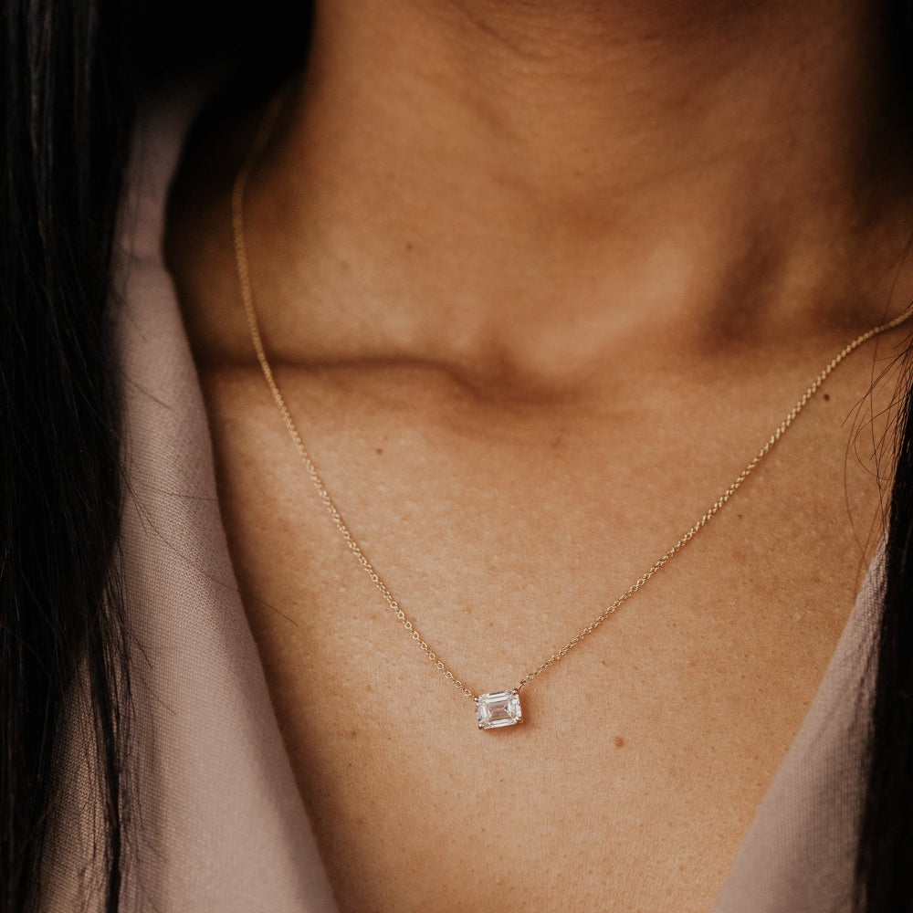 Gold necklace with a emerald cut lab grown diamond pendant on a person's neck.