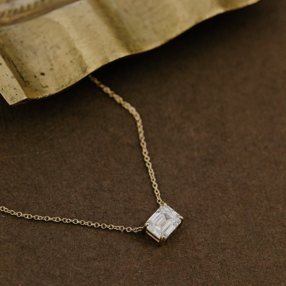 Gold necklace with a emerald cut lab grown diamond pendant on a brown surface.