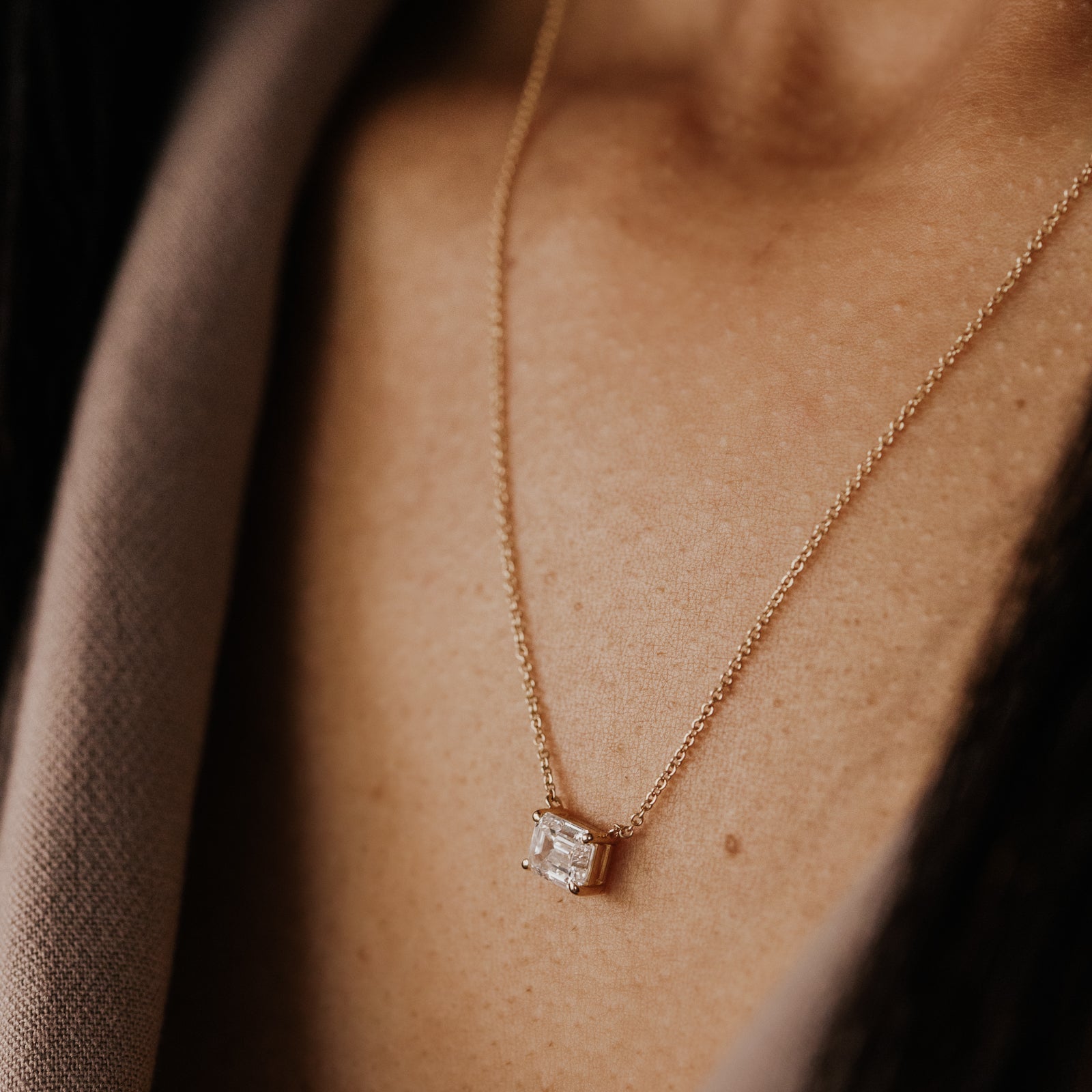 Yellow gold necklace with a emerald cut lab grown diamond pendant on a person's neck.