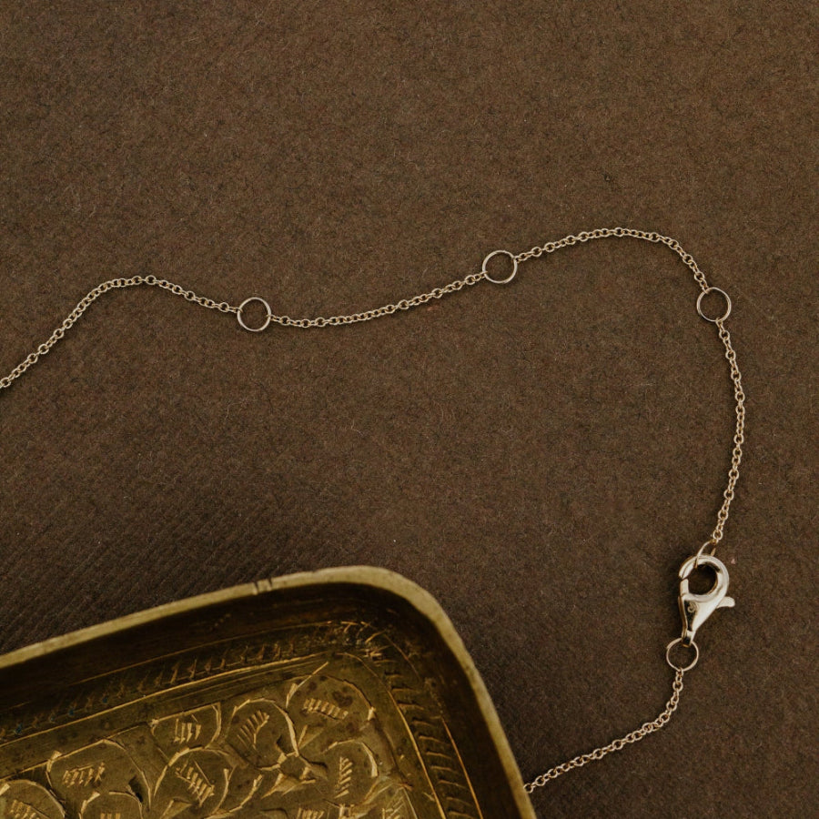 Gold chain necklace on a textured brown surface with a gold decorative object.