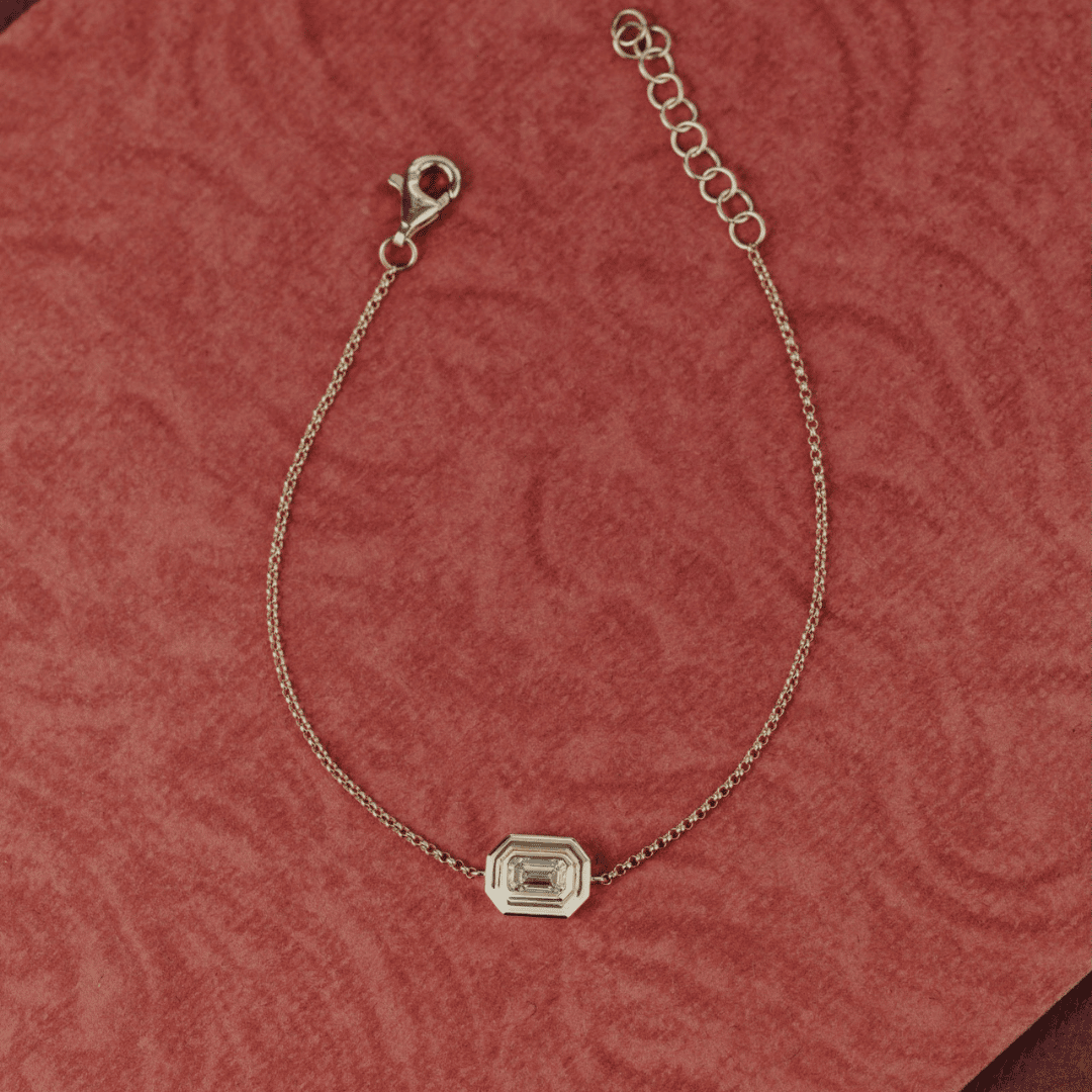 14k gold emerald cut, lab grown diamond chain bracelet showcased on a textured red surface. 