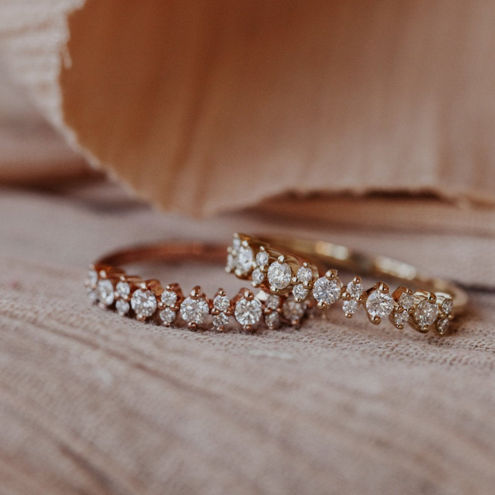 Two rings with rose gold settings, one with a larger round diamond and two smaller clear diamonds, the other with a smaller round diamond, both on a wooden surface with a beige tint.