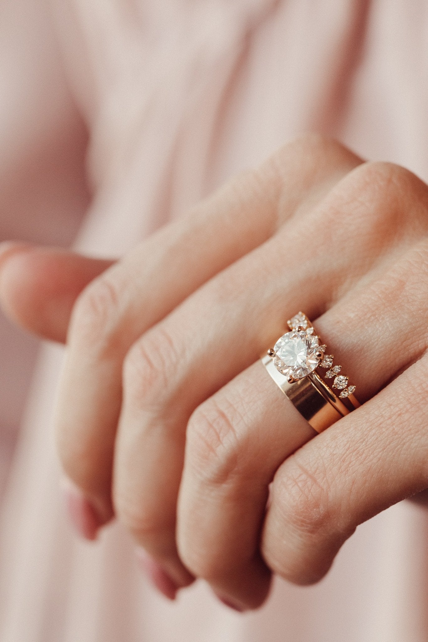 Close up of a woman wearing a 14k yellow gold diamond wedding band paired with a round diamond engagement ring and a think gold band.