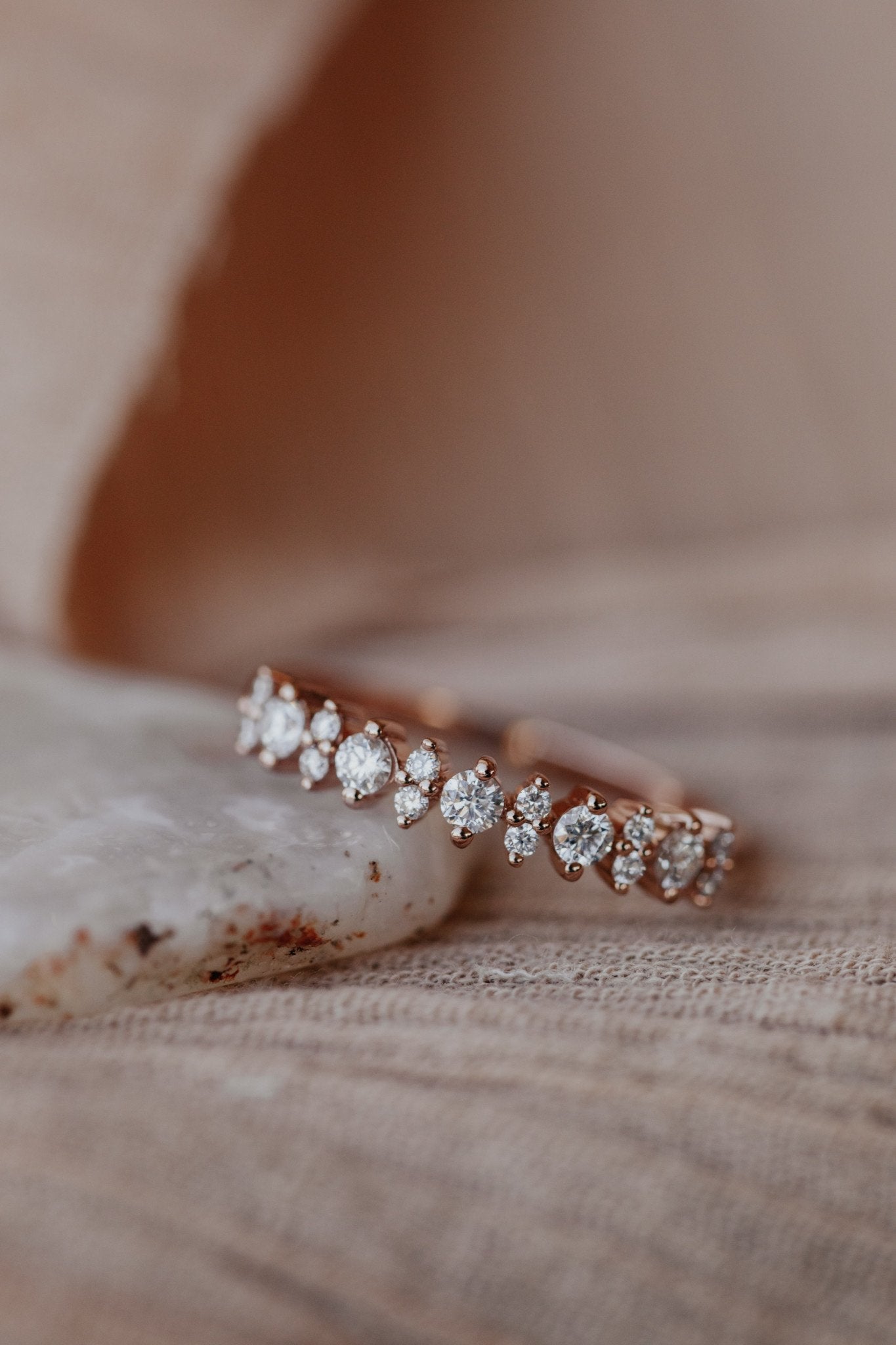 A round diamond wedding band in 14k rose gold on a textured surface.