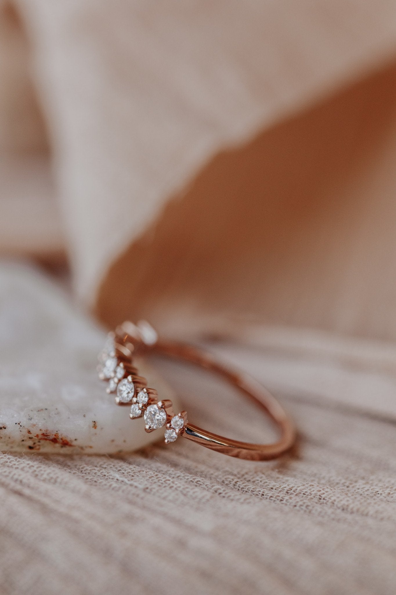 Round diamond wedding band in 14k rose gold on a textured surface.