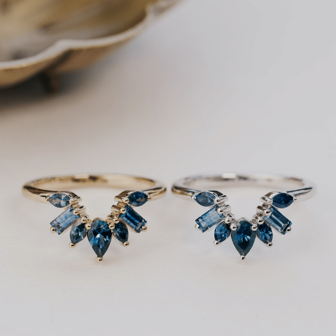 A 14k gold band-style ring with multiple sapphire stones set in a starburst design, show in yellow and white gold on a soft white surgace