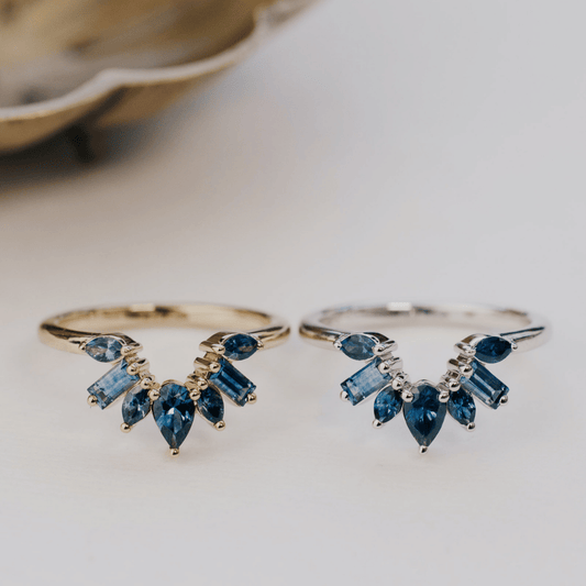 A 14k gold band-style ring with multiple sapphire stones set in a starburst design, show in yellow and white gold on a soft white surgace