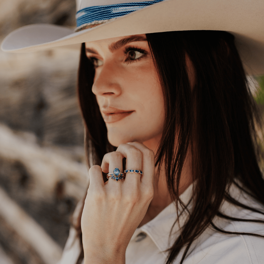 A 14k gold band-style ring with multiple sapphire stones set in a starburst design, shown on the ring finger of a hand model.