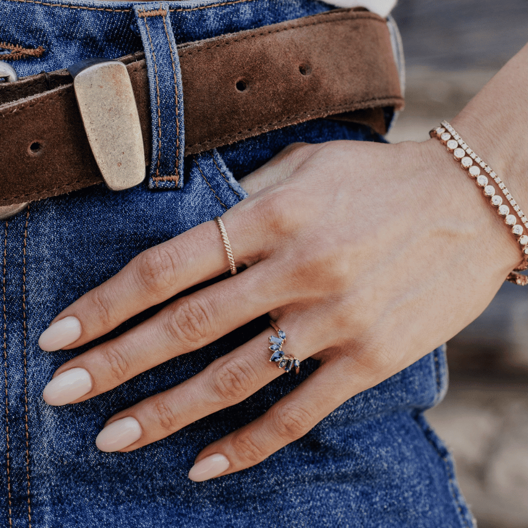 A 14k gold band-style ring with multiple sapphire stones set in a starburst design, shown on the ring finger of a hand model.