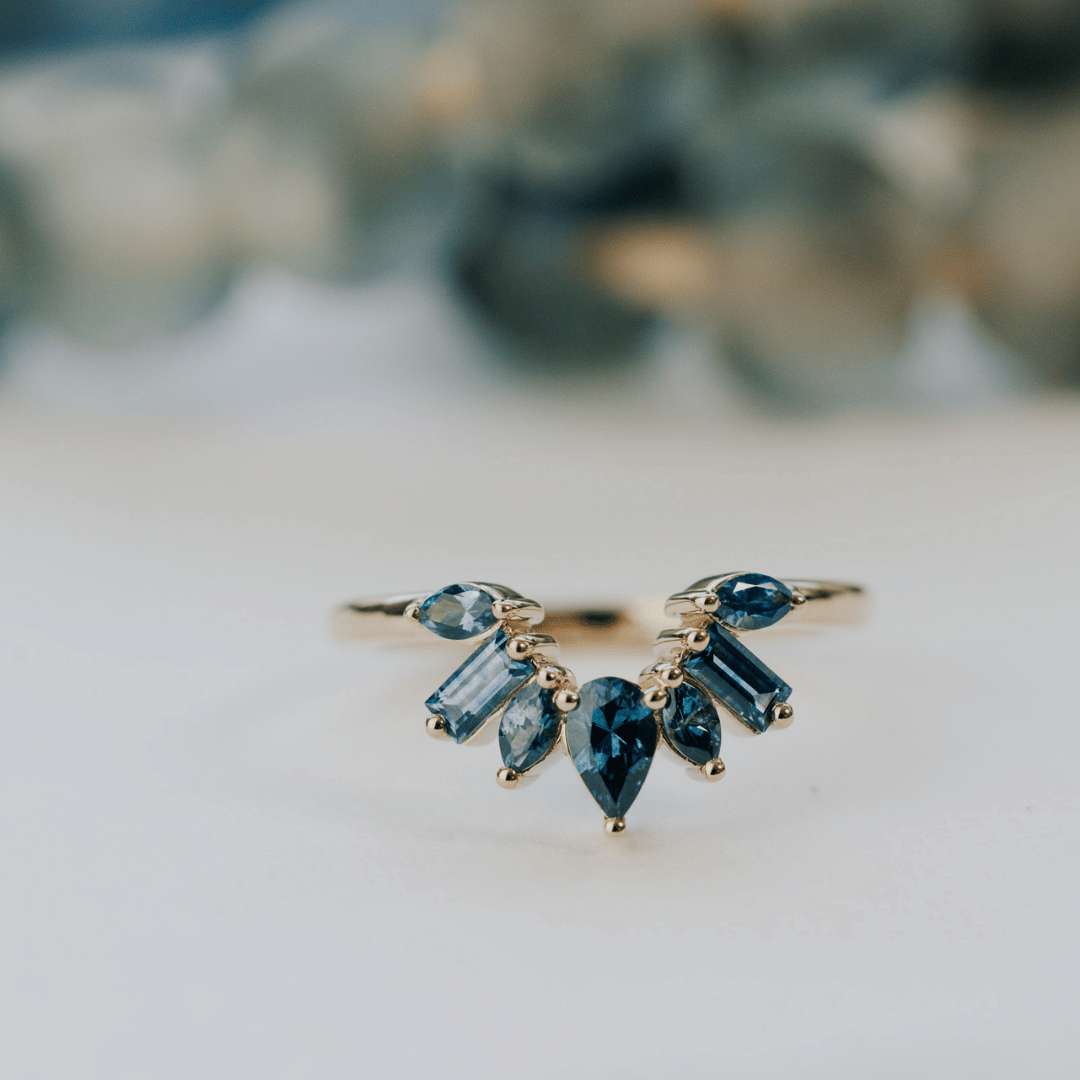A 14k gold band-style ring with multiple sapphire stones set in a starburst design, shown on a soft white surface.
