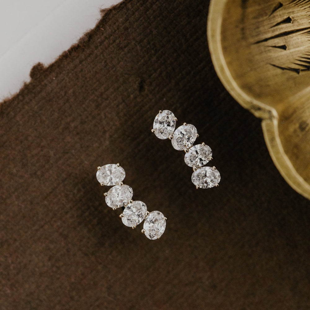 Pair of lab grown diamond stud climber earrings on a brown fabric background.
