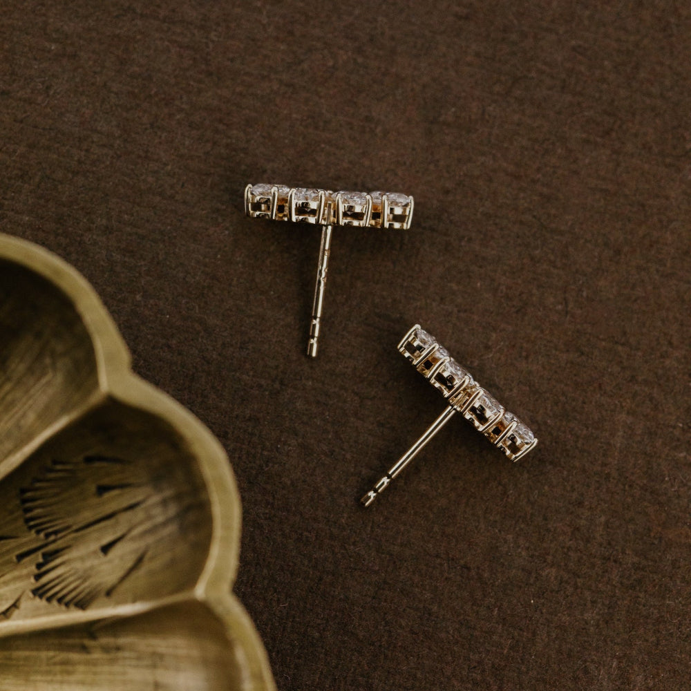 Yellow gold earrings on a brown surface with a wooden dish.