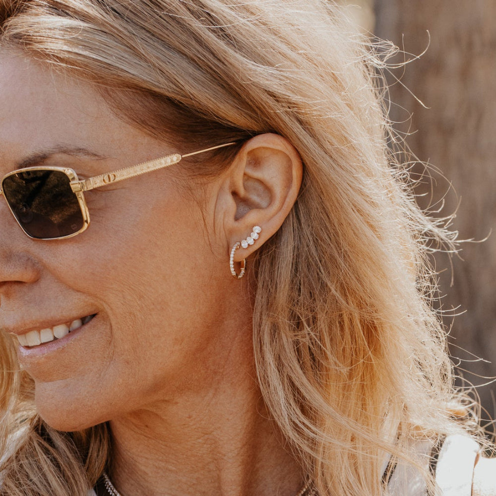 Woman wearing lab grown diamond stud climber earrings outdoors with a blurred natural background.
