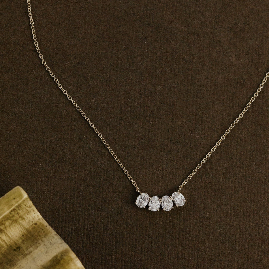 Gold necklace with four oval lab grown diamonds on a brown surface.