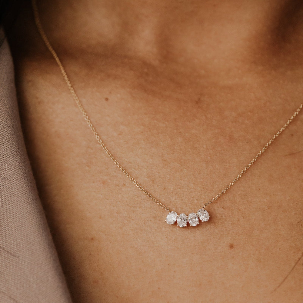 Gold necklace with four oval lab grown diamonds on a person's neck.
