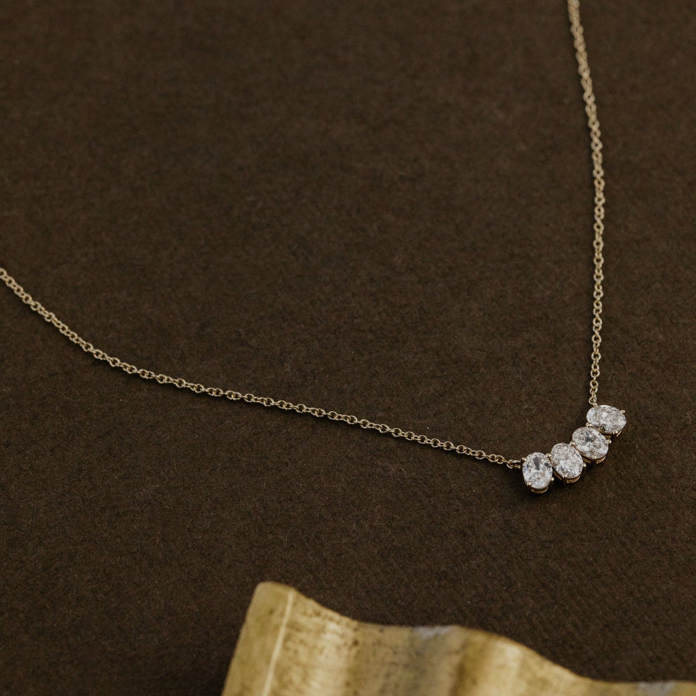 Gold necklace with four oval lab grown diamonds on a brown background.