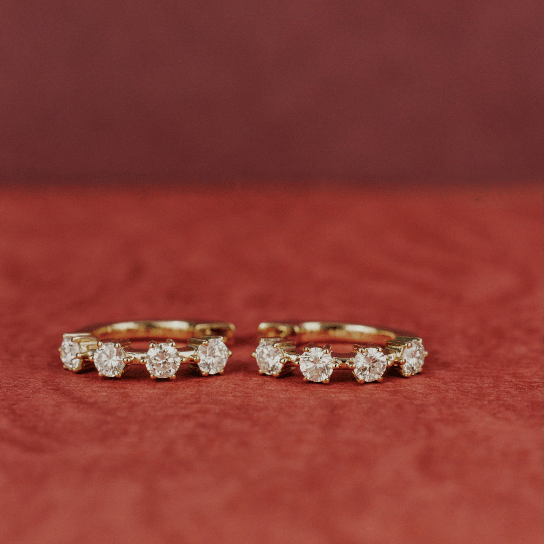 14k gold diamond 4-prong huggie earrings set showcased on a textured red surface. 