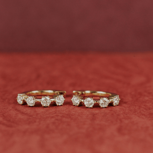14k gold diamond 4-prong huggie earrings set showcased on a textured red surface. 
