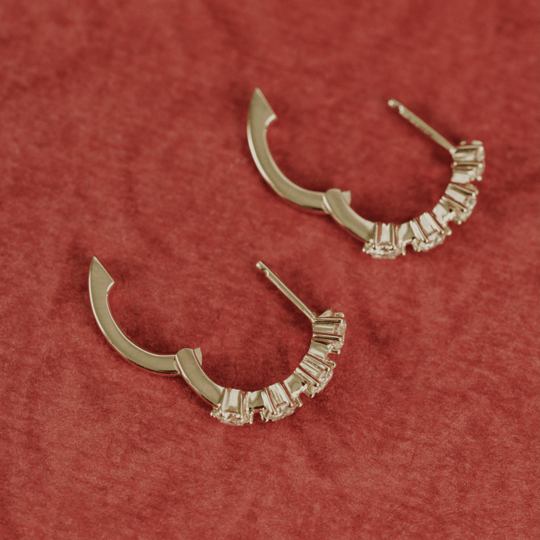 14k gold diamond 4-prong huggie earrings set showcased on a textured red surface showing the clasp open. 