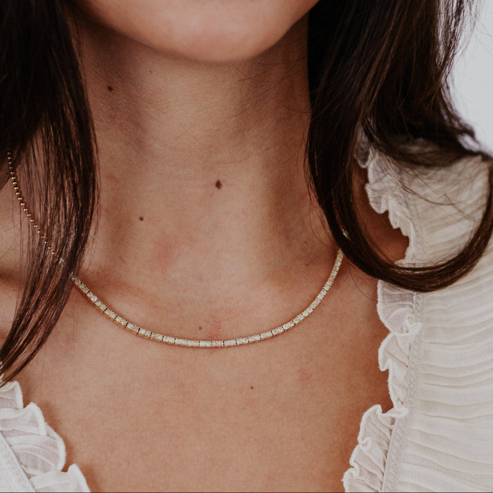 Close-up of a person wearing a delicate opal necklace with a blurred background