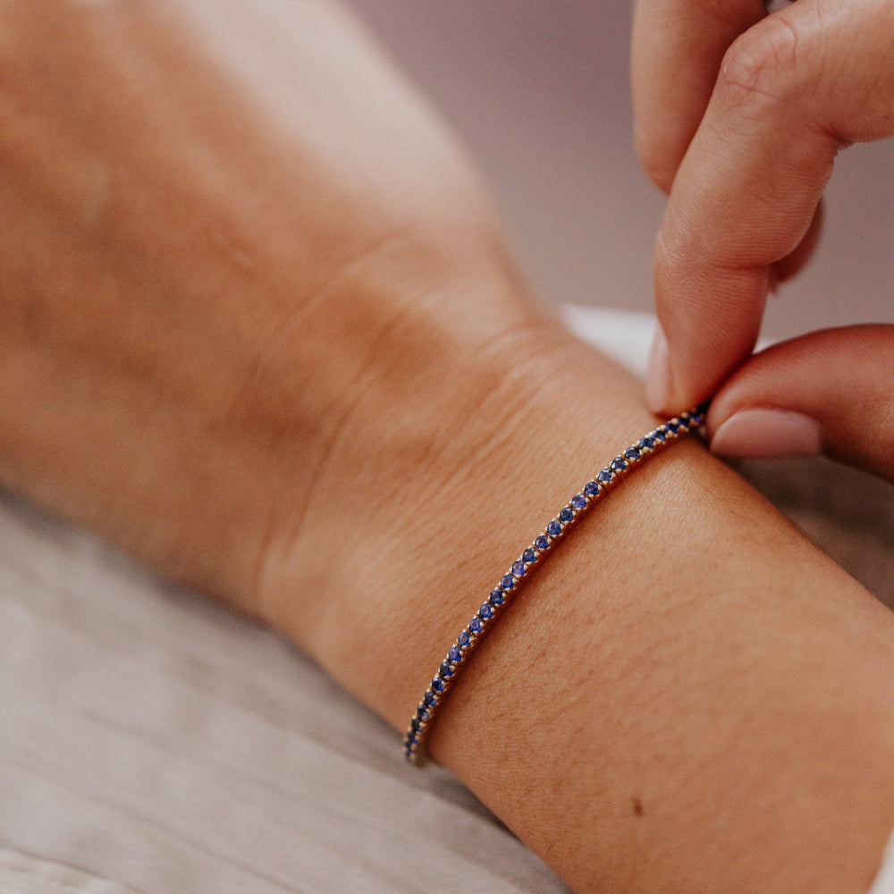 Person adjusting a sapphire paperclip bracelet on their wrist with a blurred background